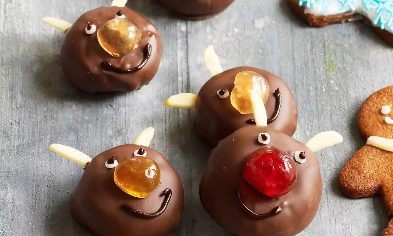 Små runde sjokoladeovertrukne konfektkaker formet som reinsdyr med mandelhorn, glasurøyne, geléaktig snute og smilende trekk på grått underlag