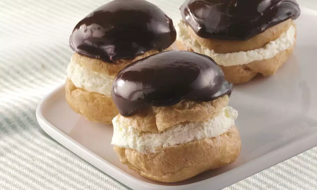 Lichtbruine soezen met een vulling van luchtige, witte slagroom en een glanzende, donkerglazige chocoladetop op een wit bord