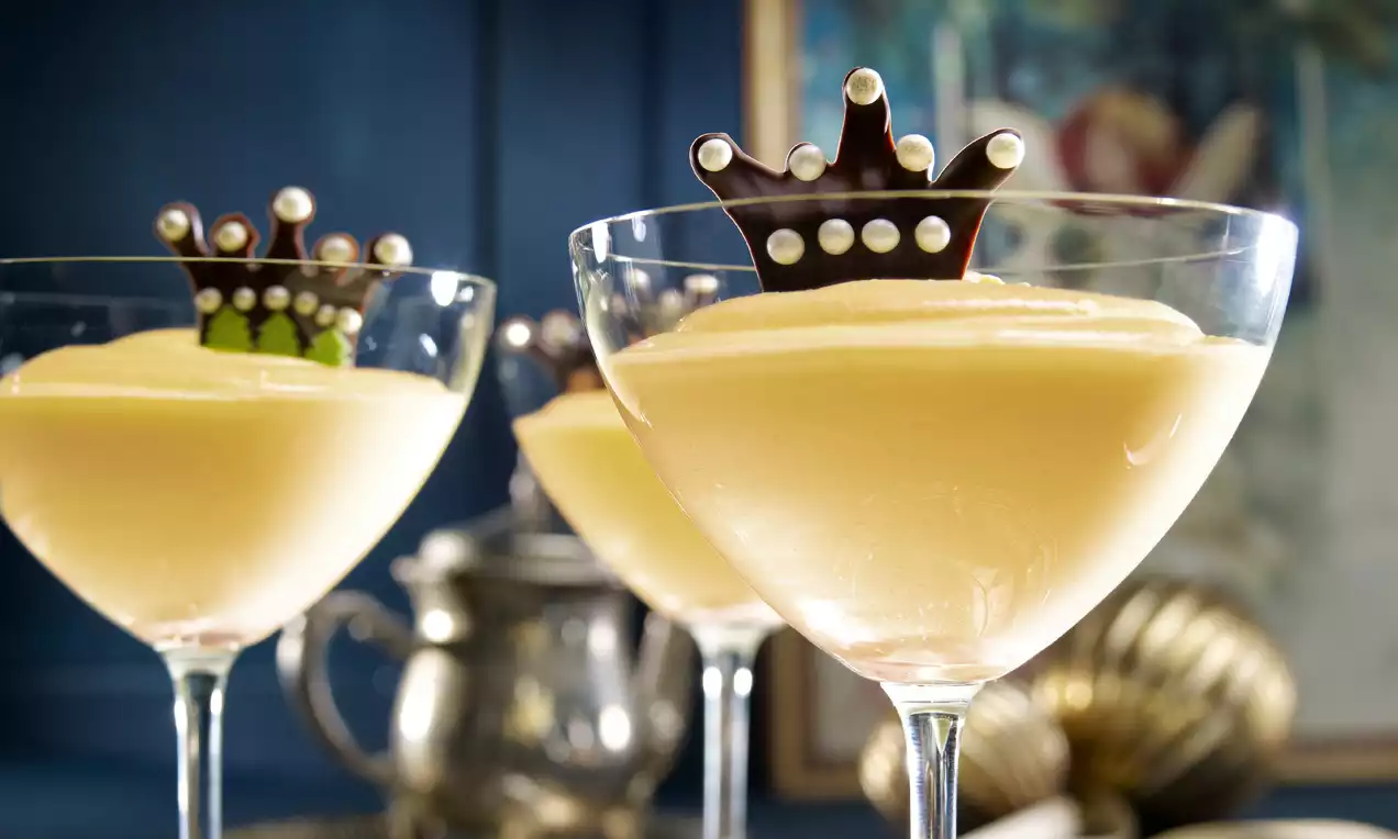 Crème jaune pâle soyeuse servie dans une coupe transparente, ornée d’une couronne chocolatée avec perles blanches