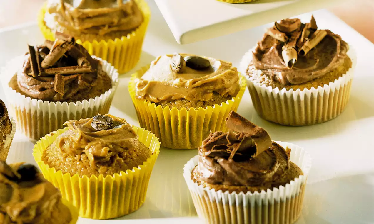 Petits gâteaux moelleux dans des caissettes en papier jaune et blanc, décorés de crème au chocolat et éclats de copeaux en spirale