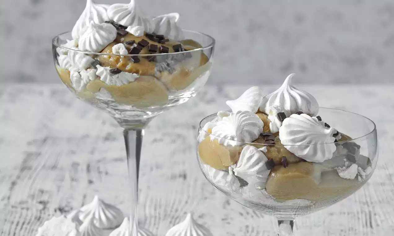 Krémově žlutý dezert ve sklenicích zdobený bílými pusinkami s jemnými hnědými kousky čokolády na světlém povrchu