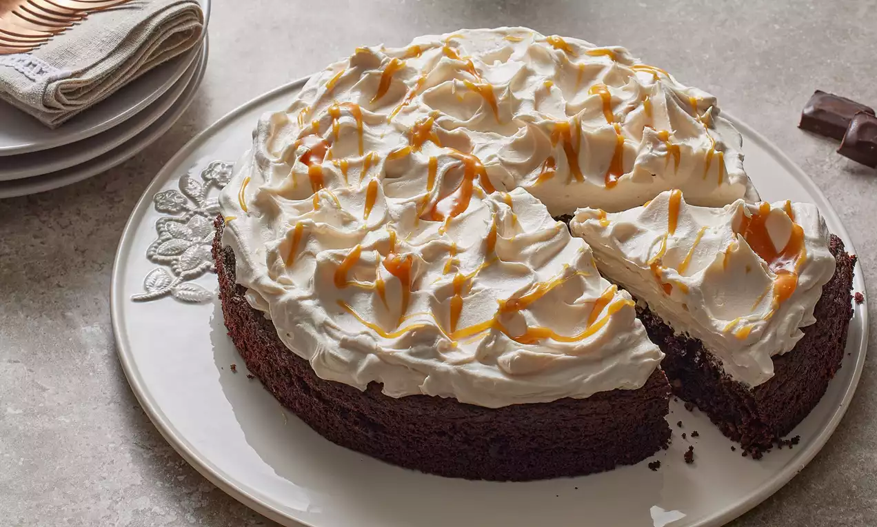 Koyu kahverengi yoğun kek tabanı üzerinde dalgalı şekilde sürülmüş kremalı beyaz kaplama ve üzerine kıvrımlı karamelli süsleme