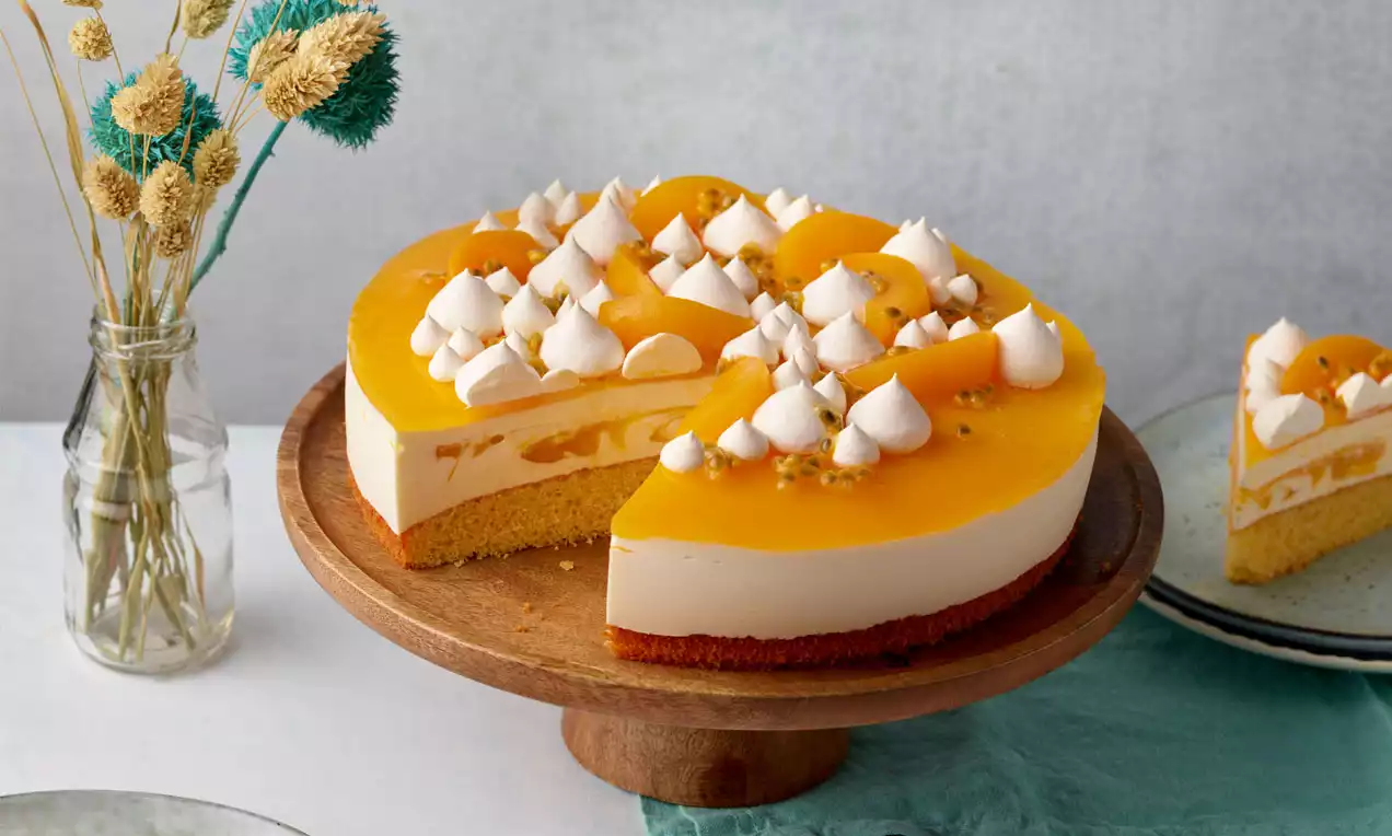 Solero®-Torte mit gelber Fruchtglasur, weißer Creme und lockerem Boden, dekoriert mit Sahnehäubchen, serviert auf rustikalem Holzständer