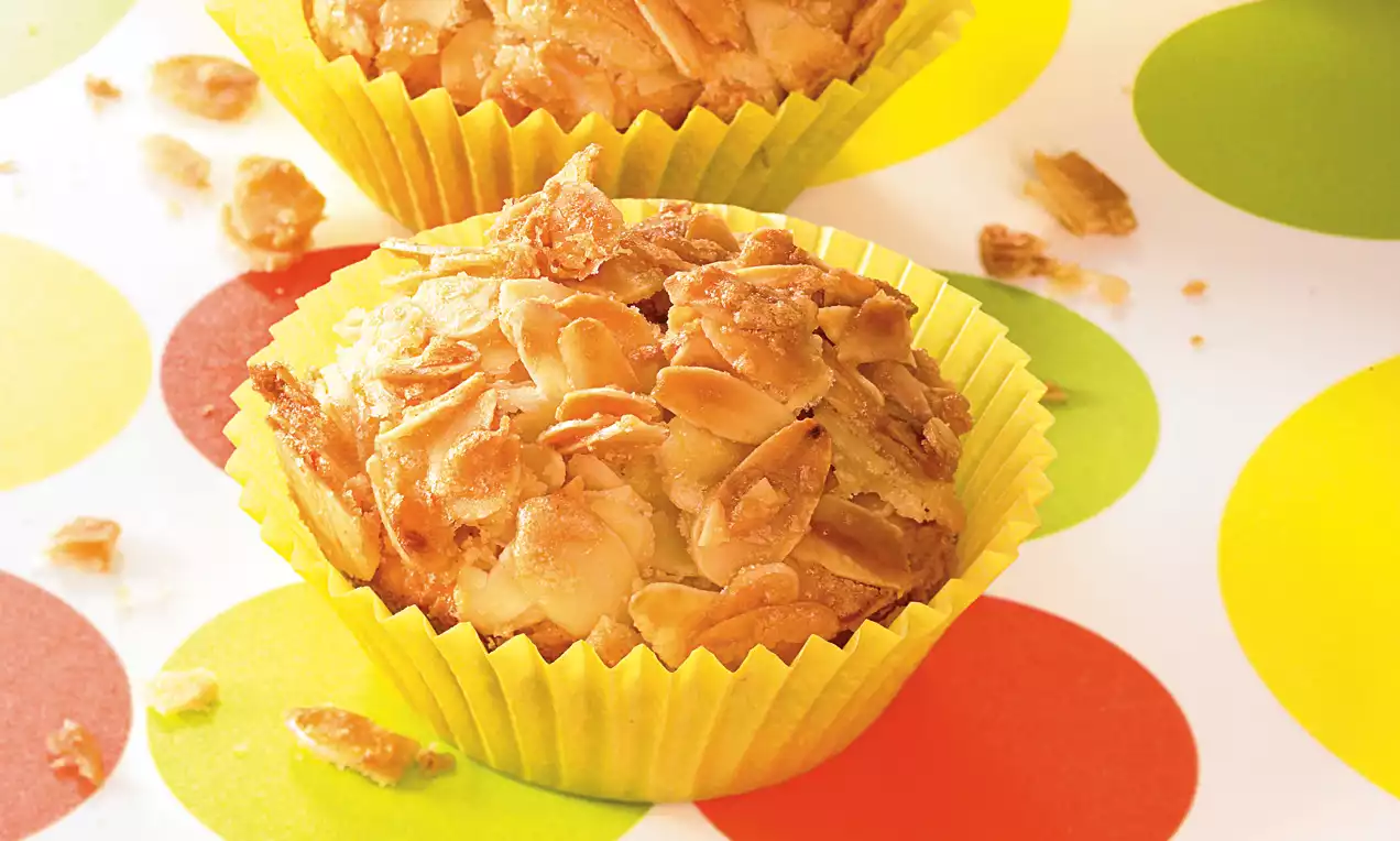 Muffins dorés parsemés d’amandes effilées croquantes dans des caissettes jaunes sur une table colorée à pois rouges, verts et jaunes
