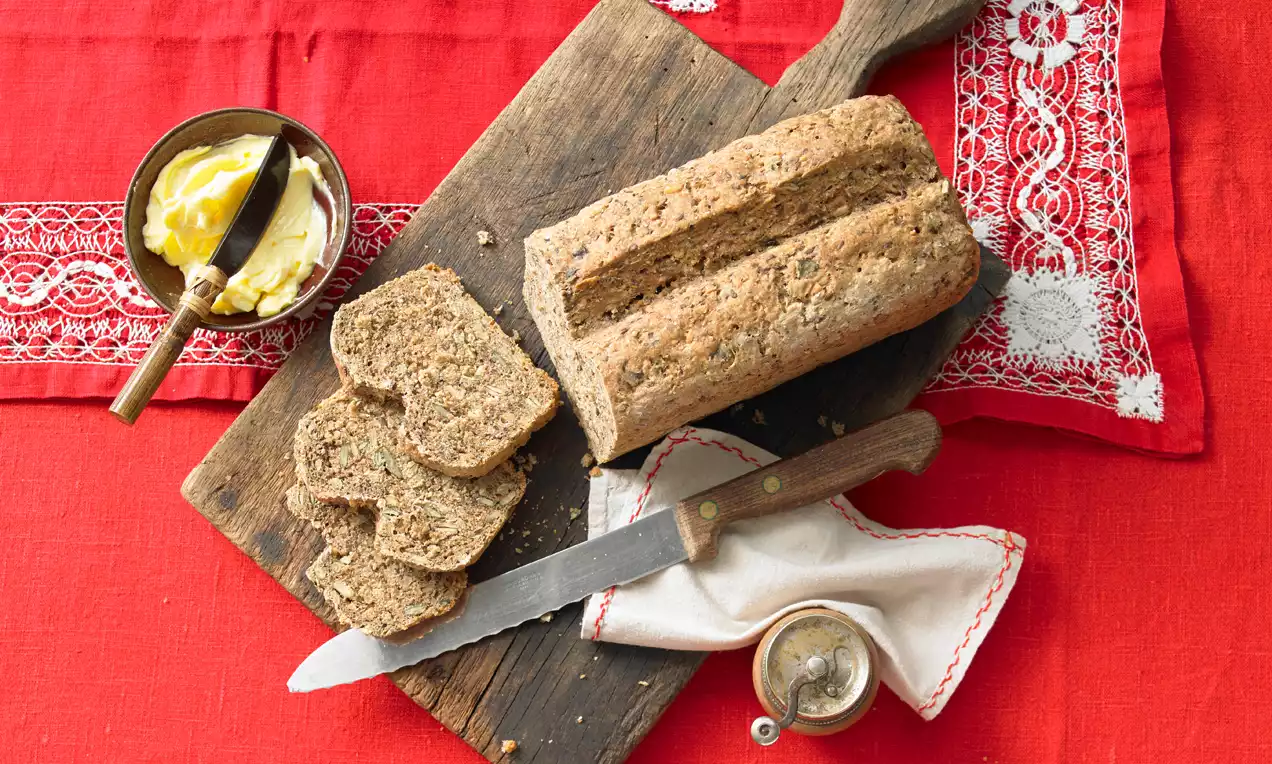Vollkornbrot mit brauner Kruste und lockerer Textur, angeschnitten und auf einem rustikalen Holzbrett mit rotem Tischtuch dekoriert