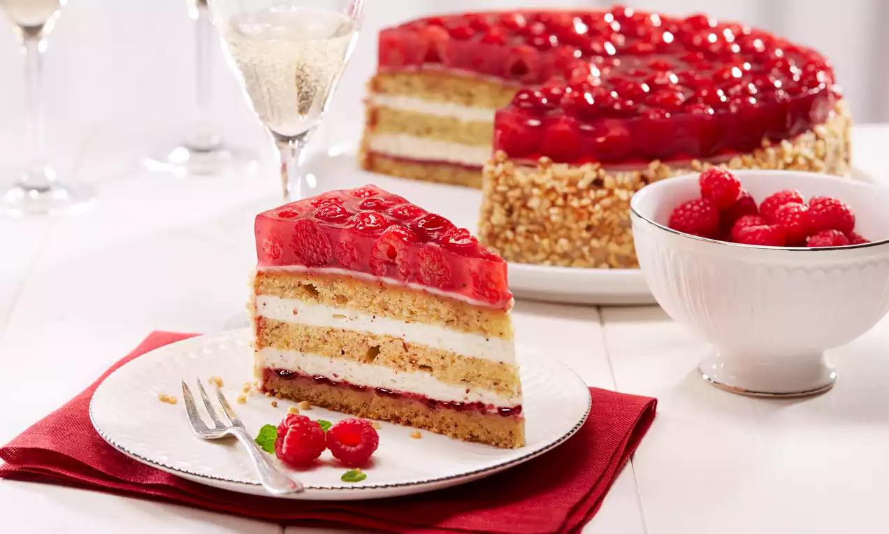 Himbeer-Nusstorte mit Schichten aus heller Creme, goldbraunem Boden und rotem Himbeer-Gelee, dekoriert mit frischen Himbeeren auf weißem Teller