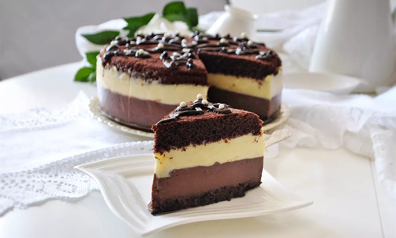 Италианска торта с шоколадови блатове, кремообразен ванилов слой, тъмна шоколадова плънка и декорация от глазура и шоколадови капки върху бяла чиния