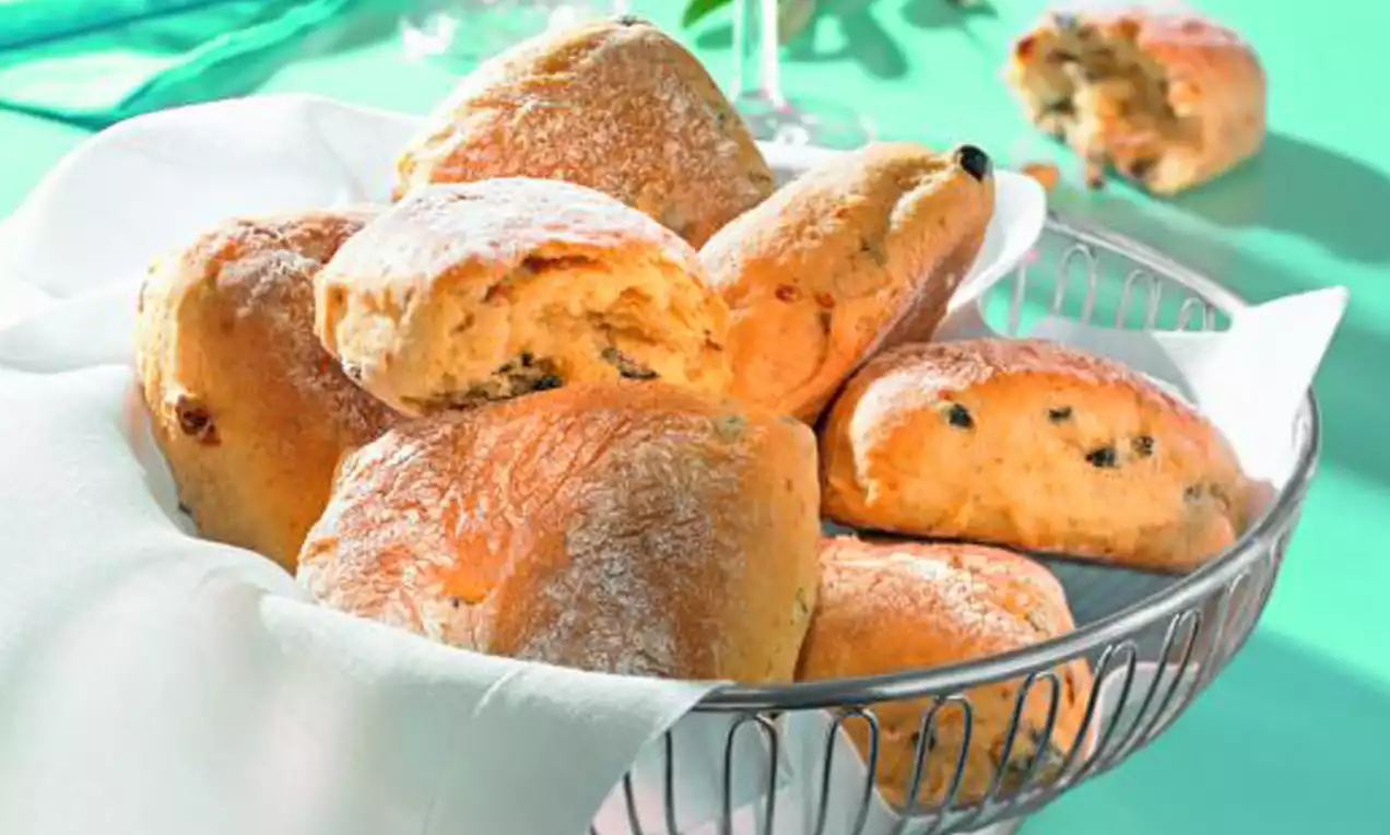 Goldbraune Ciabatta-Oliven-Brötchen mit leichter Kruste und dunklen Olivenstückchen auf weißem Tuch in einem silbernen Korb