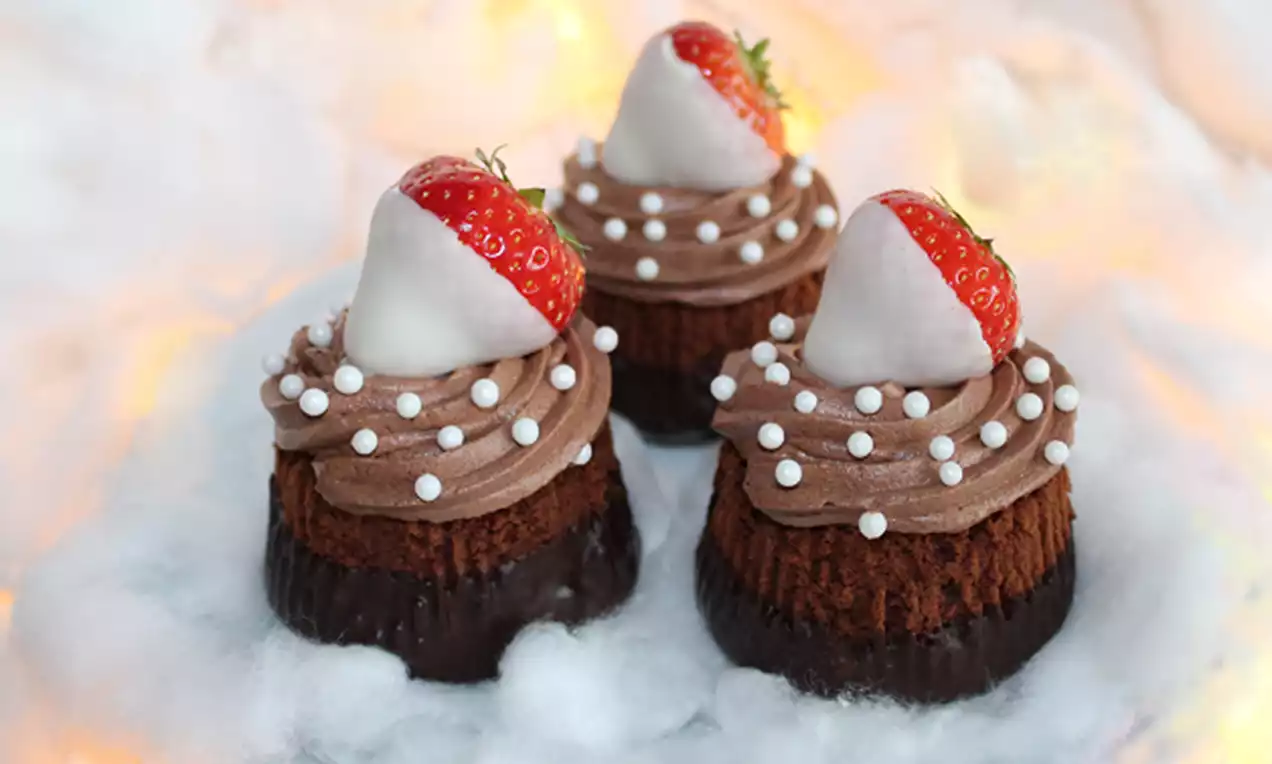 Kerstcupcakes met een luchtige chocoladebotercrème, witte chocolade-gedipte aardbeien en parels op een ondergrond van witte wolkachtige decoratie