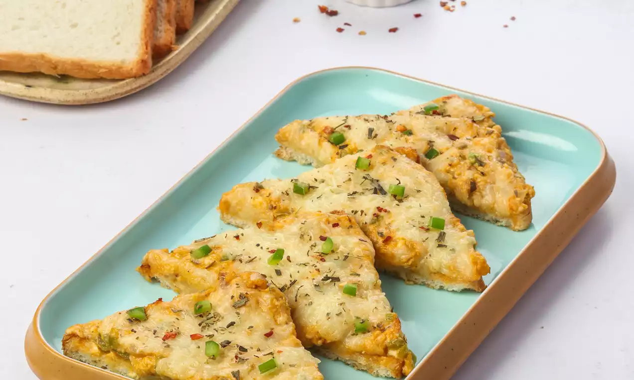 Golden triangular toast topped with melted cheese, green herbs, and red chilli bits on a pastel blue plate with bread and spice decor nearby