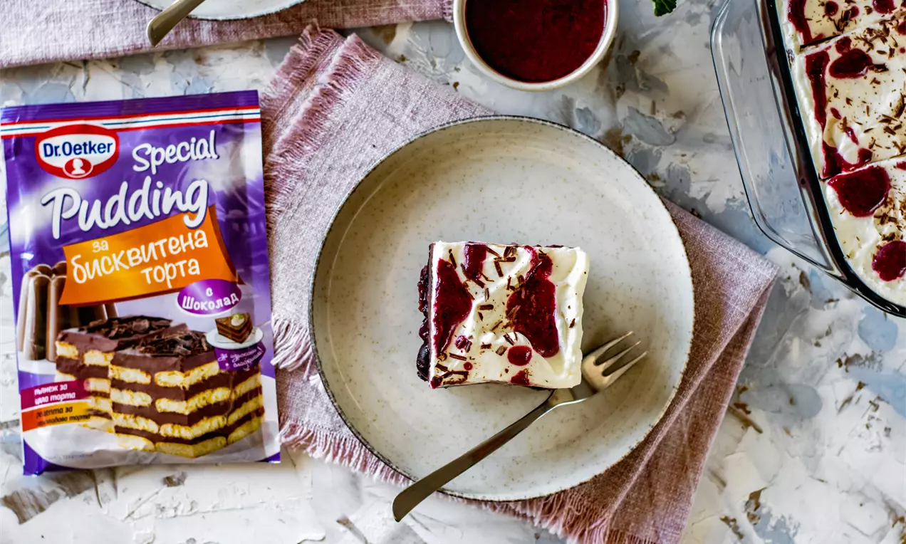 Квадратно парче десерт с бял пухкав крем, червени сочни плодови петна и шоколадови слоеве върху светла чиния с метална вилица