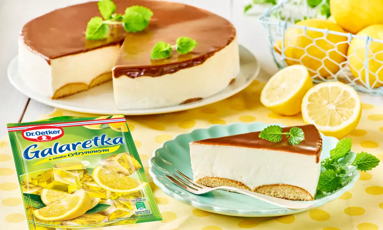 Kremowa cytrynowa pianka na jasnym biszkoptowym spodzie, pokryta gładką warstwą czekolady, udekorowana listkami świeżej mięty na pastelowym talerzu