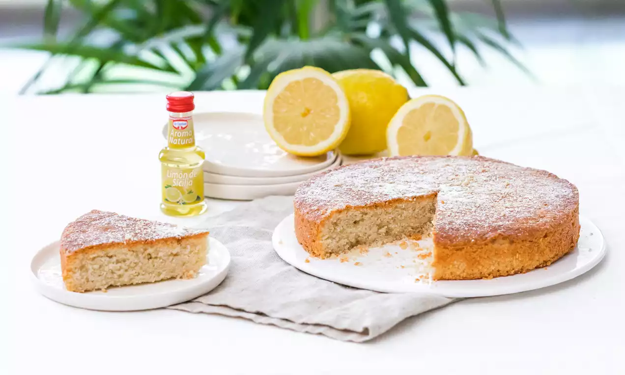 Bizcocho dorado de textura esponjosa con interior pálido, espolvoreado con azúcar glas y servido sobre platos blancos junto a limones frescos