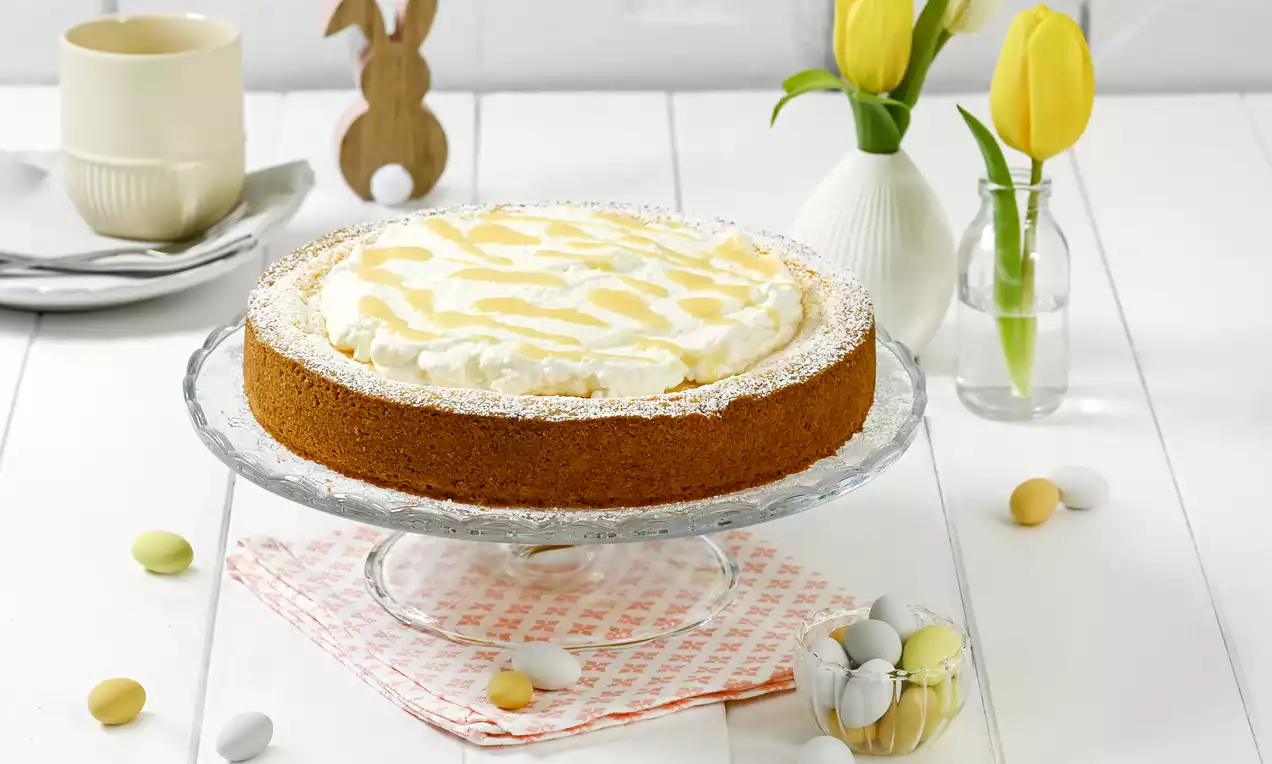 Eierlikör-Käsekuchen mit goldbrauner Kruste, weißer Sahneschicht und Eierlikörmuster auf einer Glasplatte mit Frühlingsdeko angerichtet