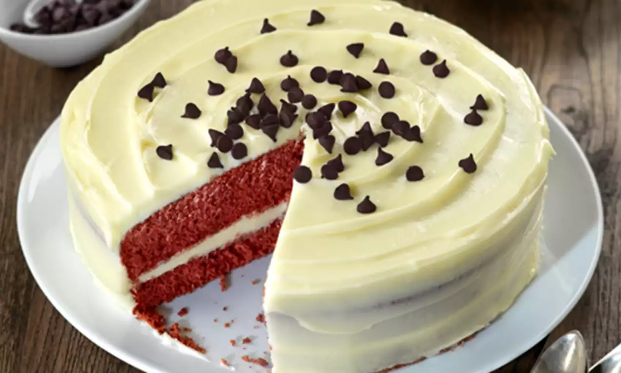 Tarta Red Velvet con capas de bizcocho rojo intenso y crema blanca suave, cubierta de chips de chocolate sobre un plato blanco