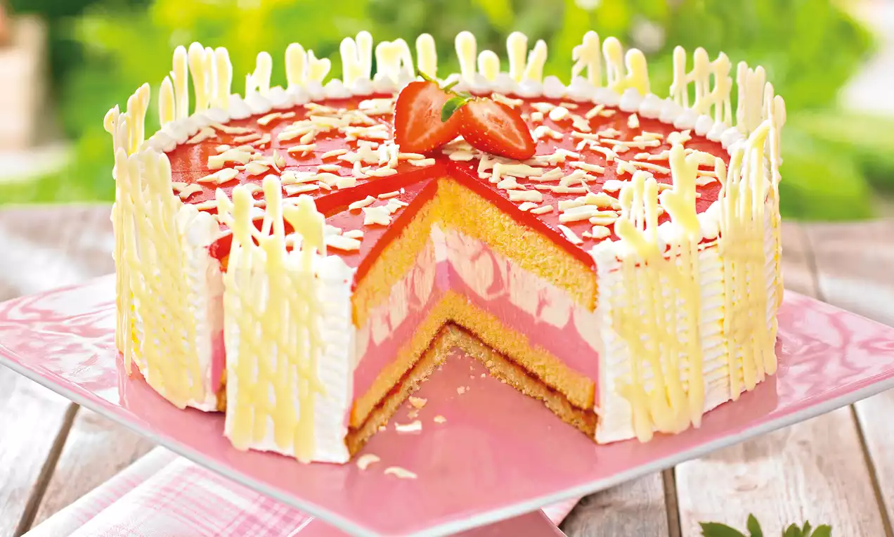 Okrugla torta s kremastim slojevima bijele i ružičaste boje, crvenim voćnim preljevom, bijelom čokoladom i jagodama na vrhu