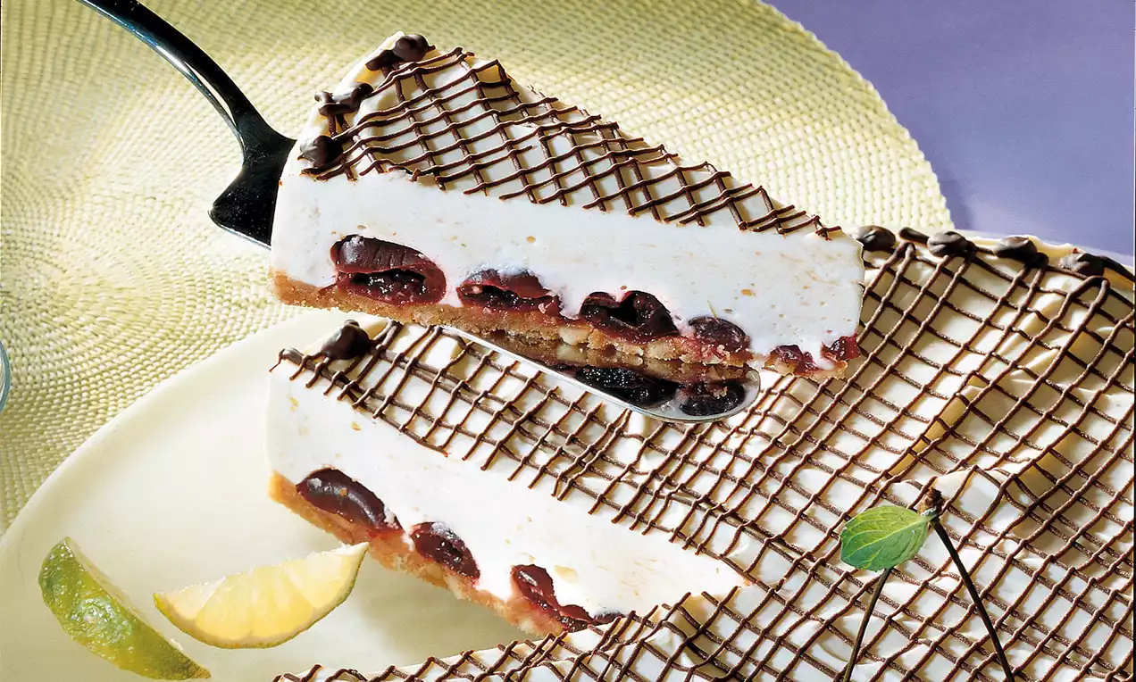 Amarena-Joghurtcremetorte mit weißer, glatter Creme und eingelegten Kirschen auf braunem Boden, verziert mit feinen Schokoladenstreifen