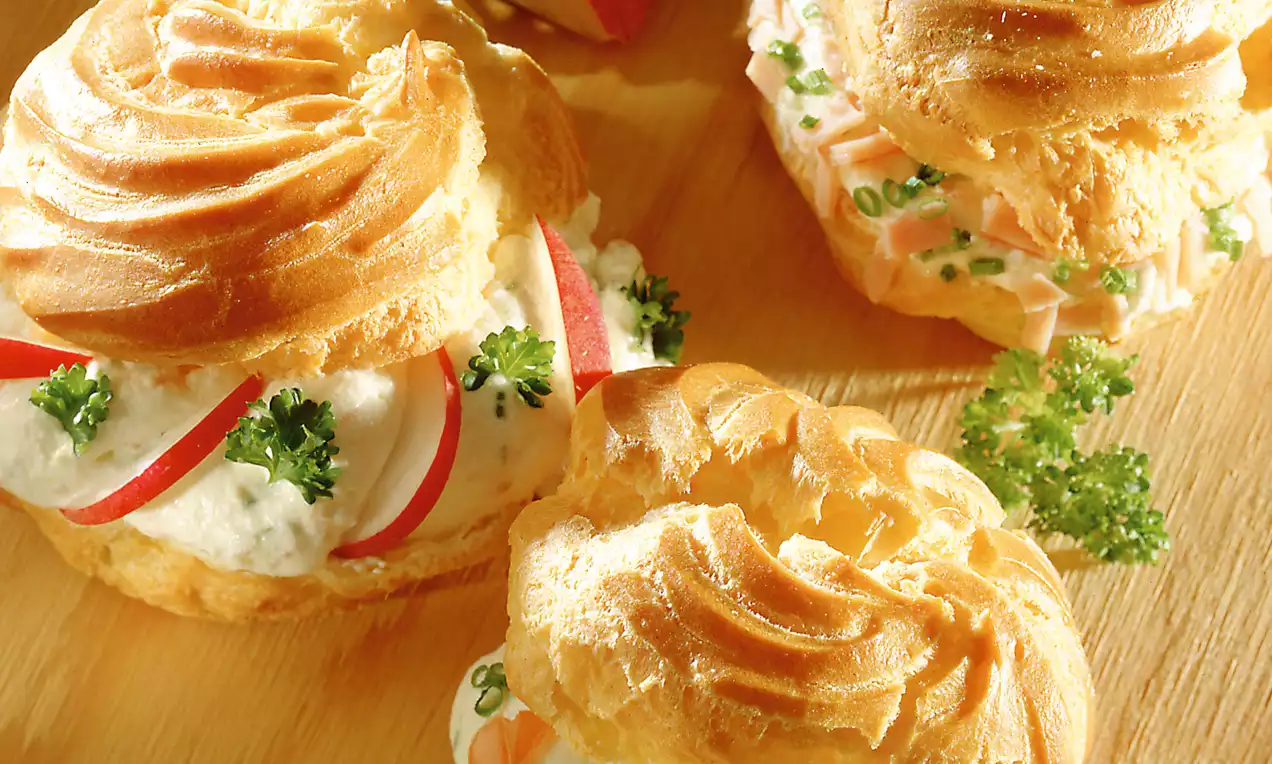 Goldbraune, gebräunte Krapferln aus Brandteig, gefüllt mit cremiger, heller Pikantmasse, dekoriert mit Radieschen, Lachs und Kräutern