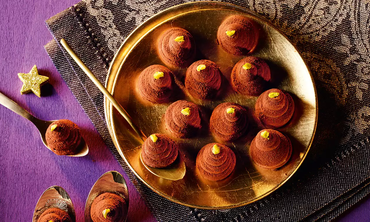 Petits cônes en chocolat brun au sommet poudré de cacao et parés d’une touche dorée sur une assiette dorée avec des cuillères