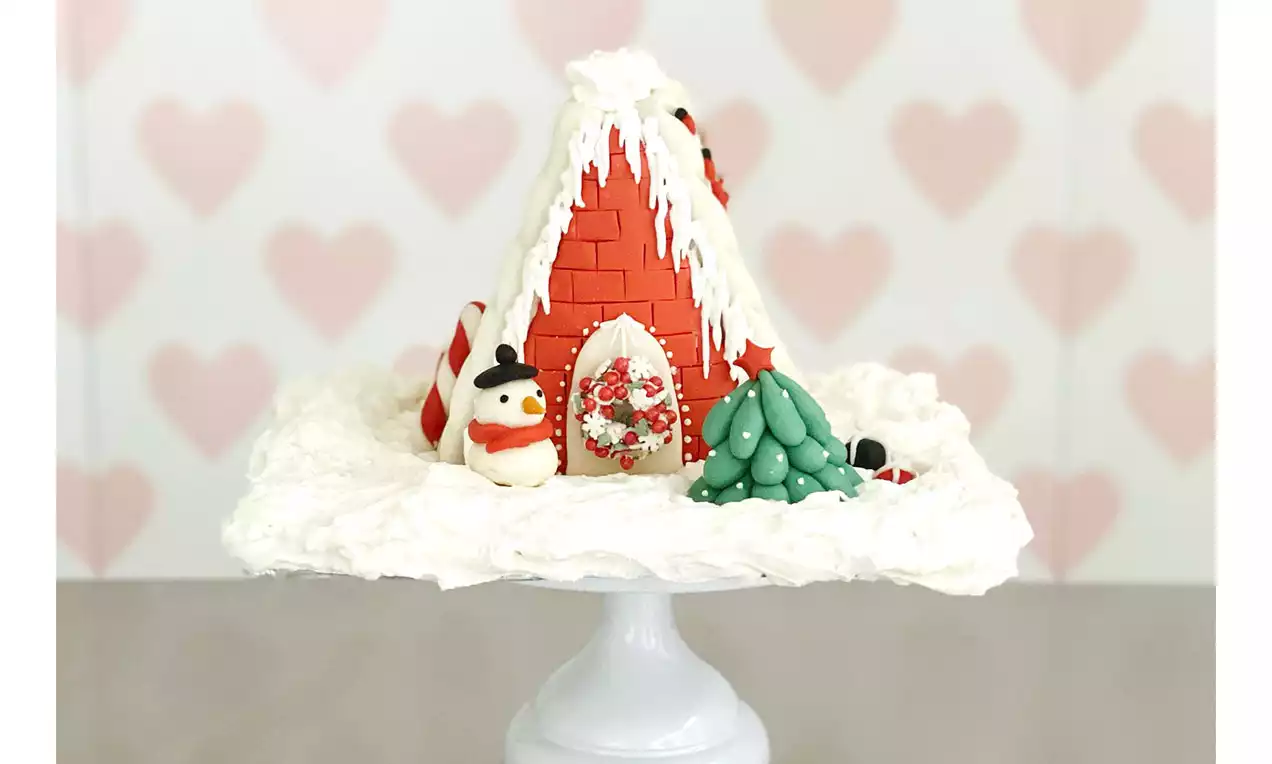 Knusperhäuschen aus roten Zuckermauersteinen mit weißer Zuckerglasur, dekoriert mit Schneemann, Baum und Süßigkeiten auf schneeweißem Untergrund