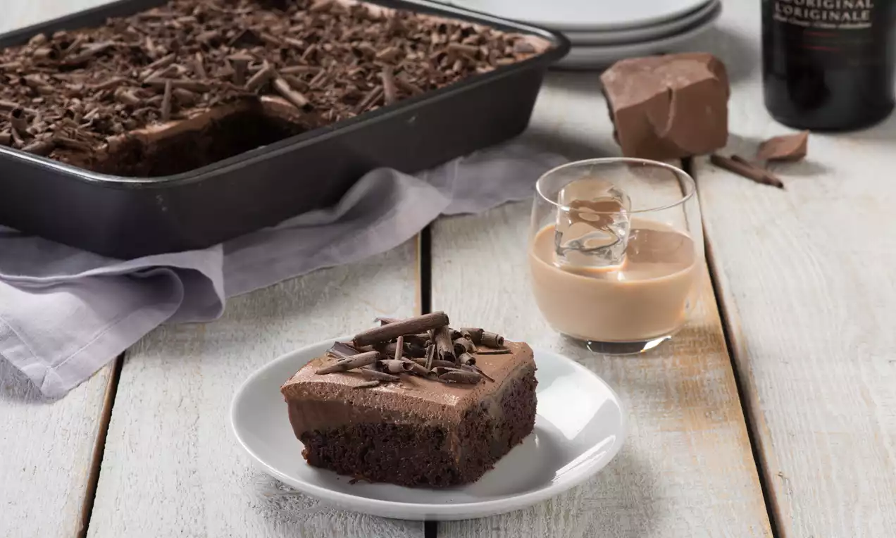 Carré de gâteau moelleux couleur cacao surmonté d’une crème brun clair et de copeaux de chocolat, servi sur une assiette blanche