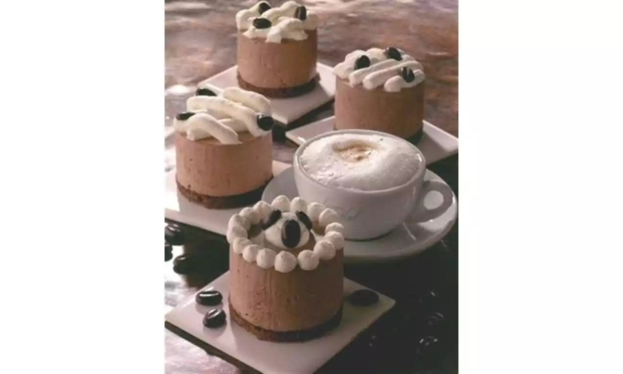 Petits gâteaux mousseux couleur café sur bases croustillantes, couronnes de crème blanche garnies de grains de café accompagnés d'une tasse cappuccino