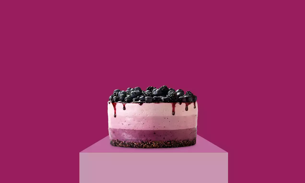 Triple-layer cheesecake with ombre shades of pink and purple, topped with glossy whole blueberries and berry syrup drips