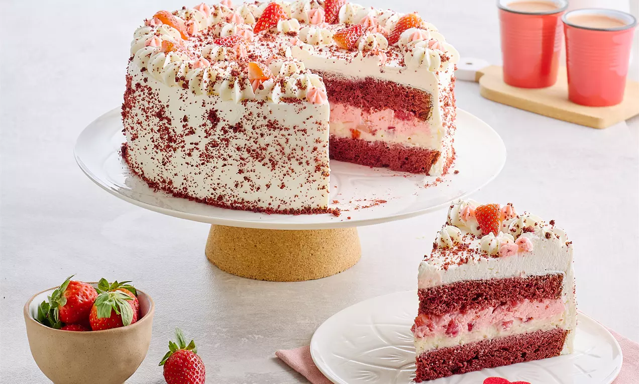 Kırmızı kadife katmanları ve krema dolgulu, çileklerle süslenmiş, beyaz servis tabağında bir dilimi ayrılmış romantik pasta