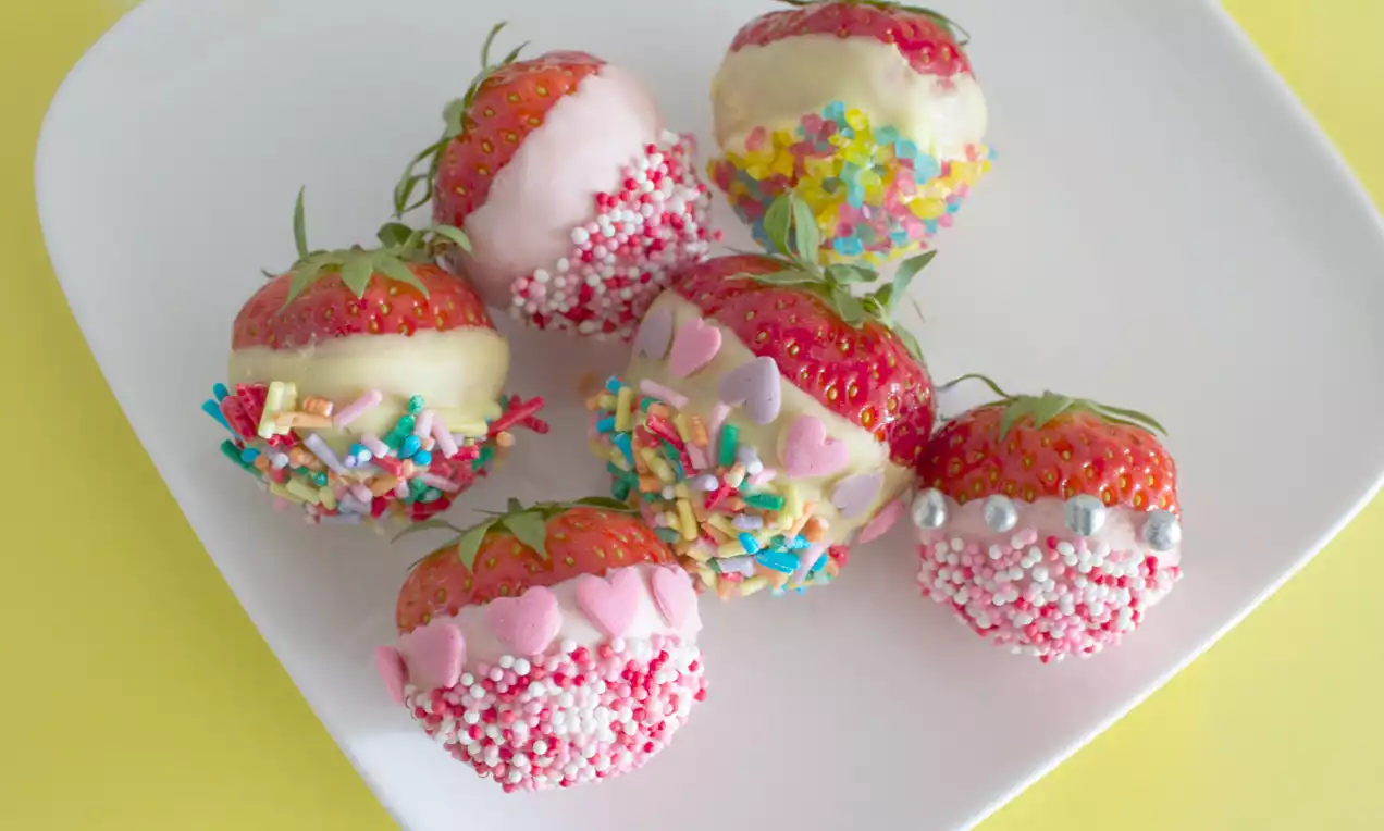 Rode aardbeien met groene kroontjes, gedoopt in witte of roze chocolade en versierd met kleurrijke strooisels op een wit bord