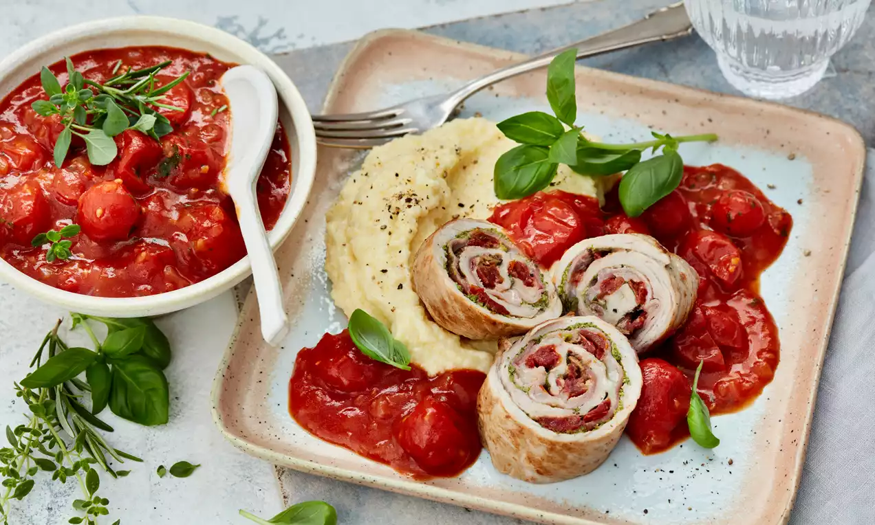 Dünn geschnittene Involtini mit Kräuterfüllung, goldbraun gebraten, auf cremigem Kartoffelpüree und roten Tomatensugo, garniert mit Basilikum