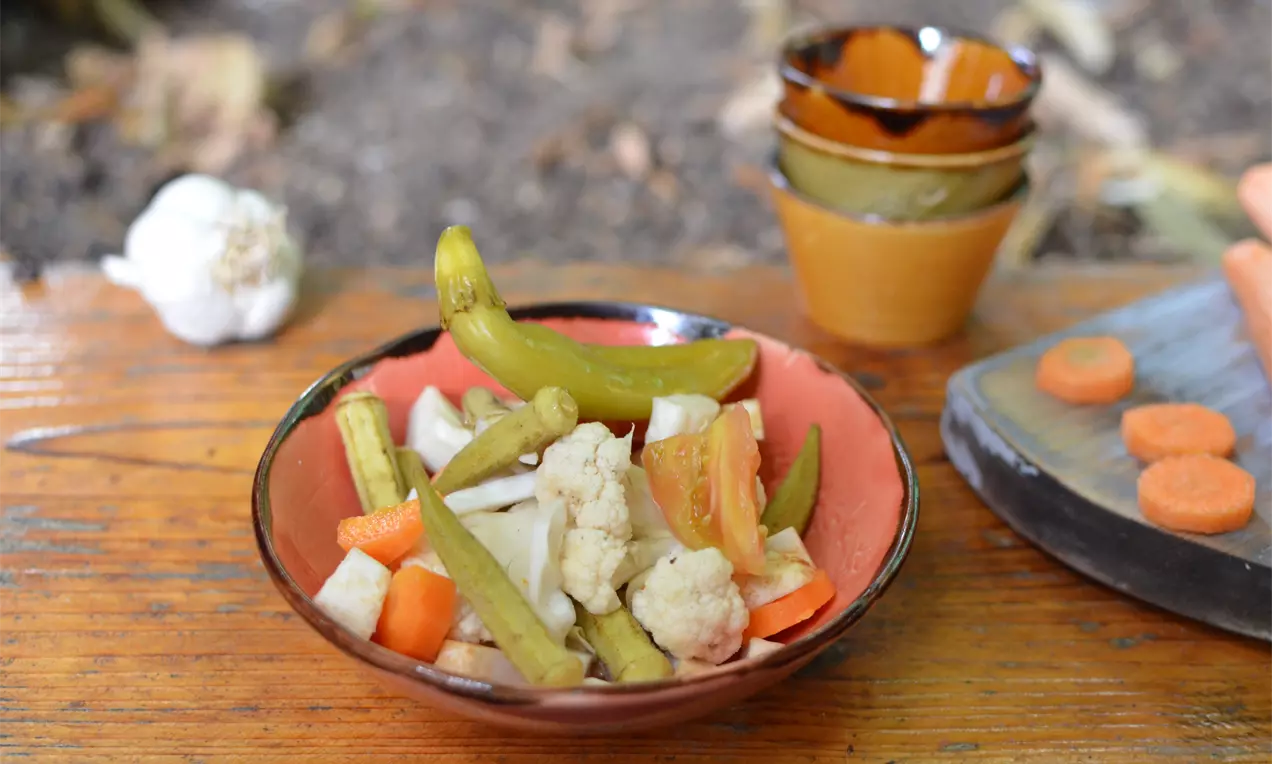 Пъстра смес от зелени чушки, карфиол и моркови с горчица, наредени в червеникава купа върху дървена маса на открито