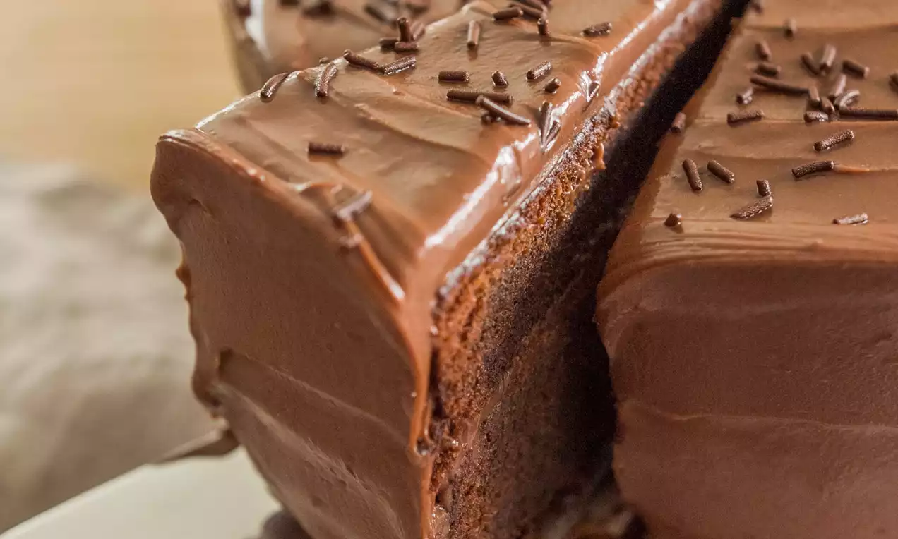 Pastel circular cubierto de crema de chocolate brillante con migas oscuras, una rebanada cortada sobre espátula en plato claro