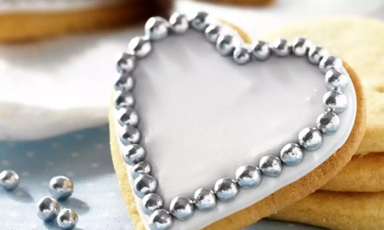 Biscuit en forme de cœur recouvert de glaçage blanc lisse et bordé de perles argentées brillantes sur un fond à pois bleus