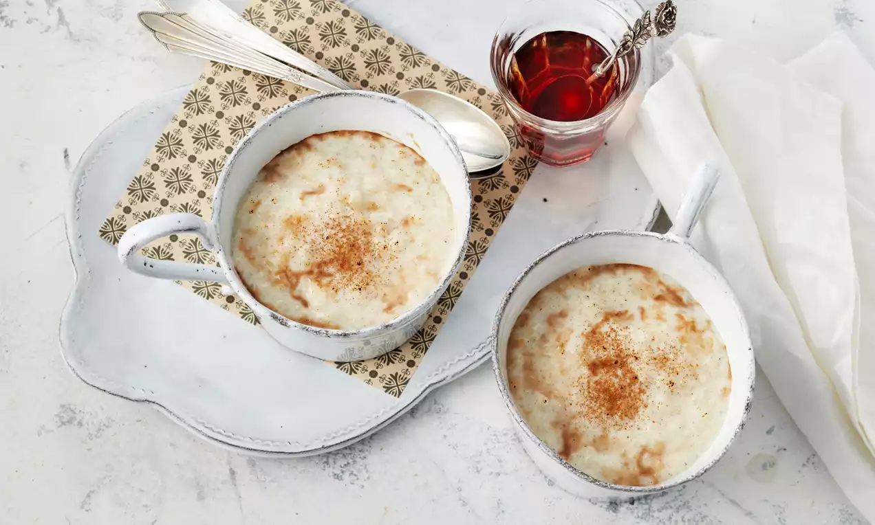 Türkischer Milchreis mit heller, cremiger Oberfläche, goldbrauner Zimtschicht in weißen Schalen auf einem Tablett mit Tee und Besteck