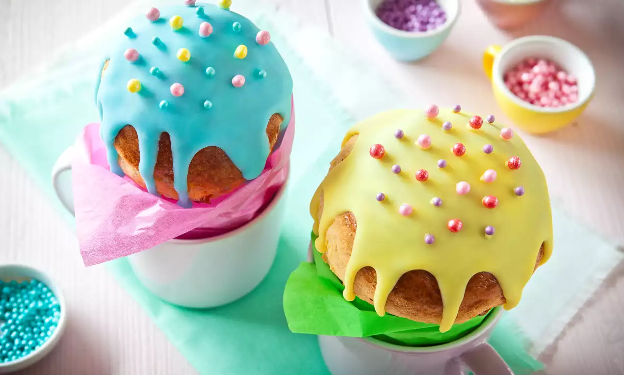 Babka w kształcie grzybka z lukrem żółtym i błękitnym oraz kolorowymi cukrowymi perełkami, podana w filiżankach z kolorową bibułą