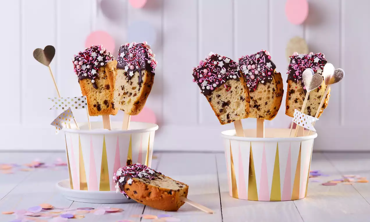 Lollies de gâteau marbré dorés sur bâtonnets, trempés dans du chocolat noir décoré de paillettes sucrées roses et blanches dans des pots rayés colorés