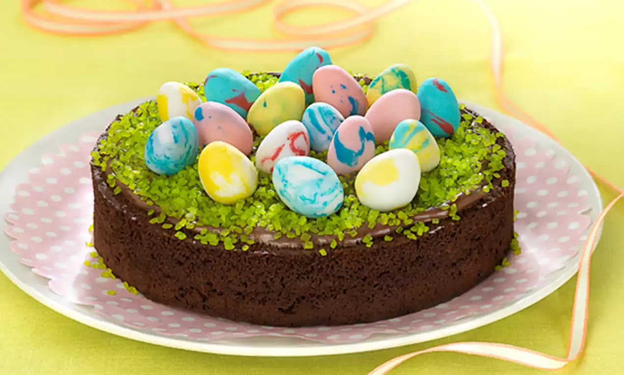Tarta de chocolate oscuro con textura compacta, cubierta con grageas verdes brillantes y huevos decorados de fondant en colores vivos
