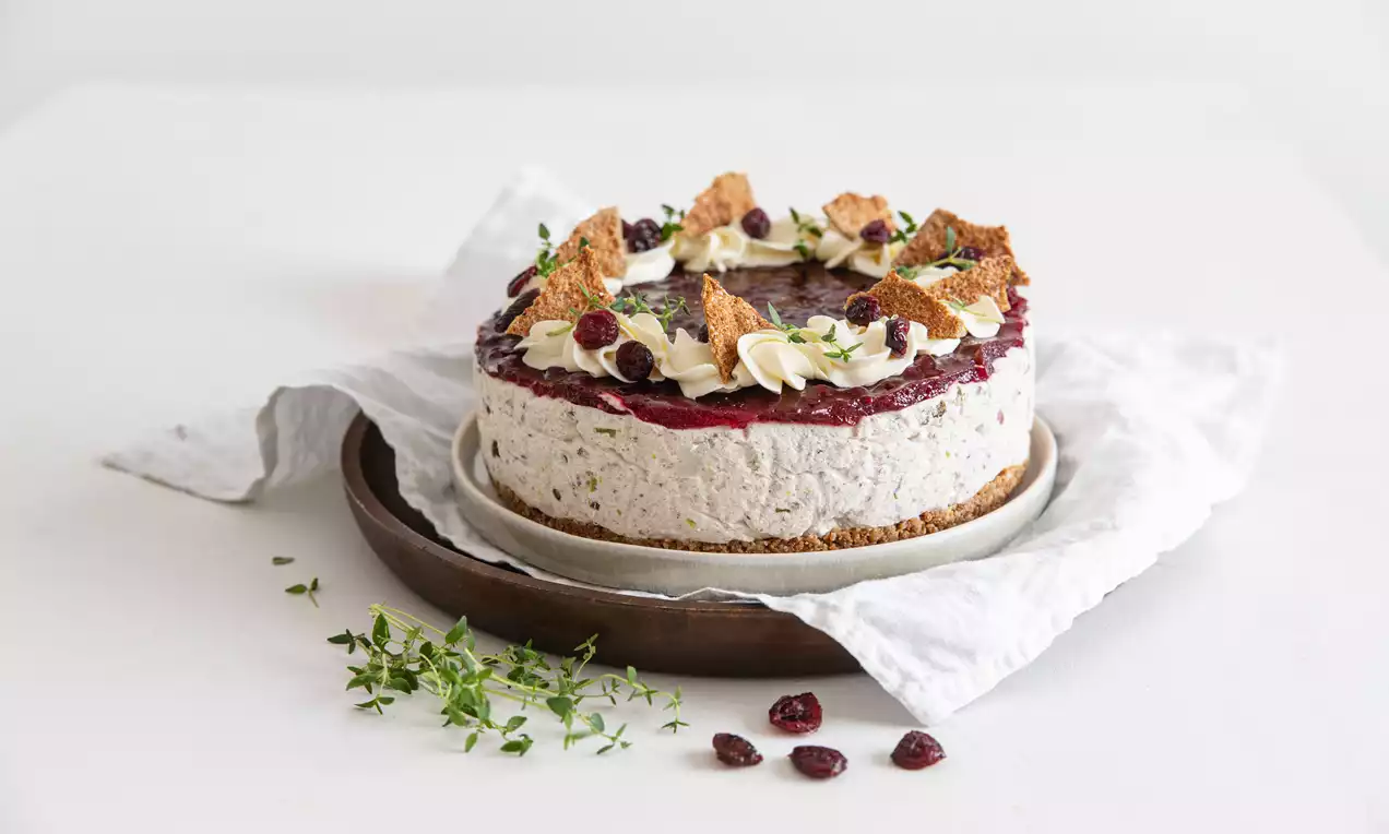 Pyöreä voileipäkakku tasaisella porotäytteellä, tummanpunaisella hyytelöpinnalla, koristeena kermaruusukkeita, leipäruutuja ja timjamia valkoisella liinalla