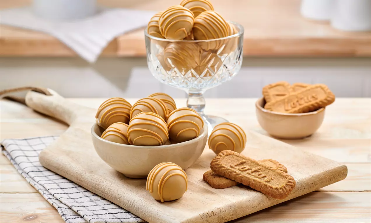 Truffes rondes au caramel clair avec des lignes en relief, servies dans un bol crème sur une planche en bois avec des biscuits Lotus
