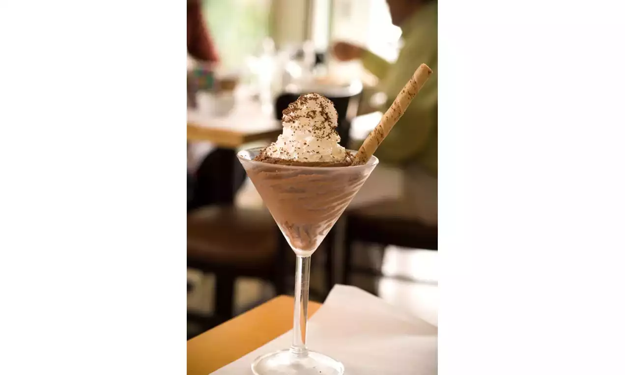 Chocolate mousse swirled in a martini glass topped with whipped cream, chocolate shavings, and a beige rolled wafer stick