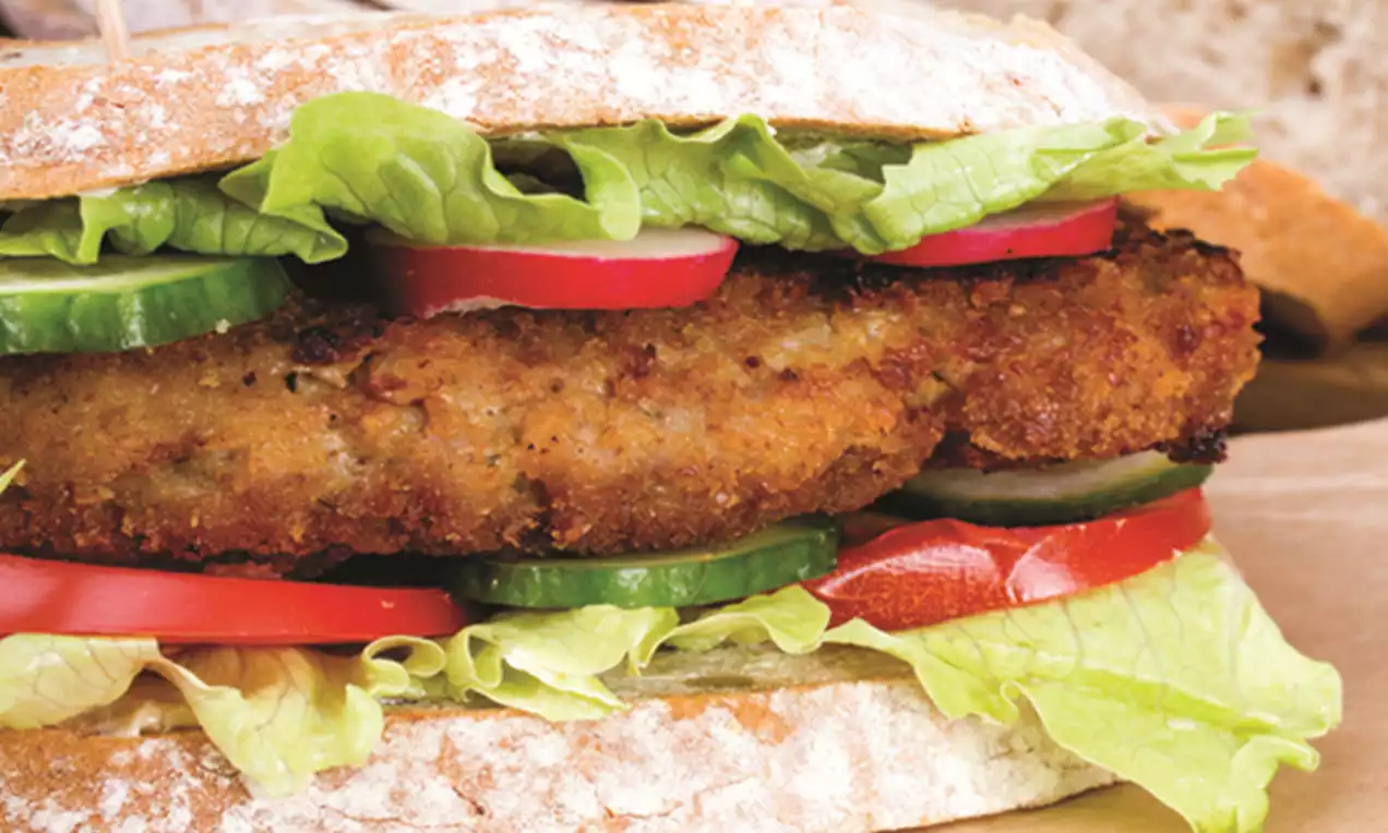 Golden, crispy fried chicken fillet nestled in sliced cucumbers, red radishes, lettuce, and tomatoes between rustic bread