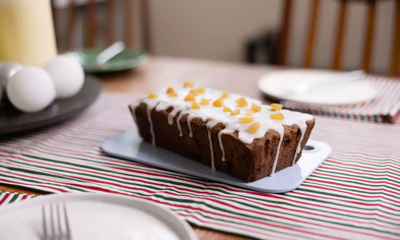 Cake rectangulaire brun moelleux parsemé de pépites de chocolat, nappé de glaçage blanc et décoré de morceaux de fruits jaunes opalescents