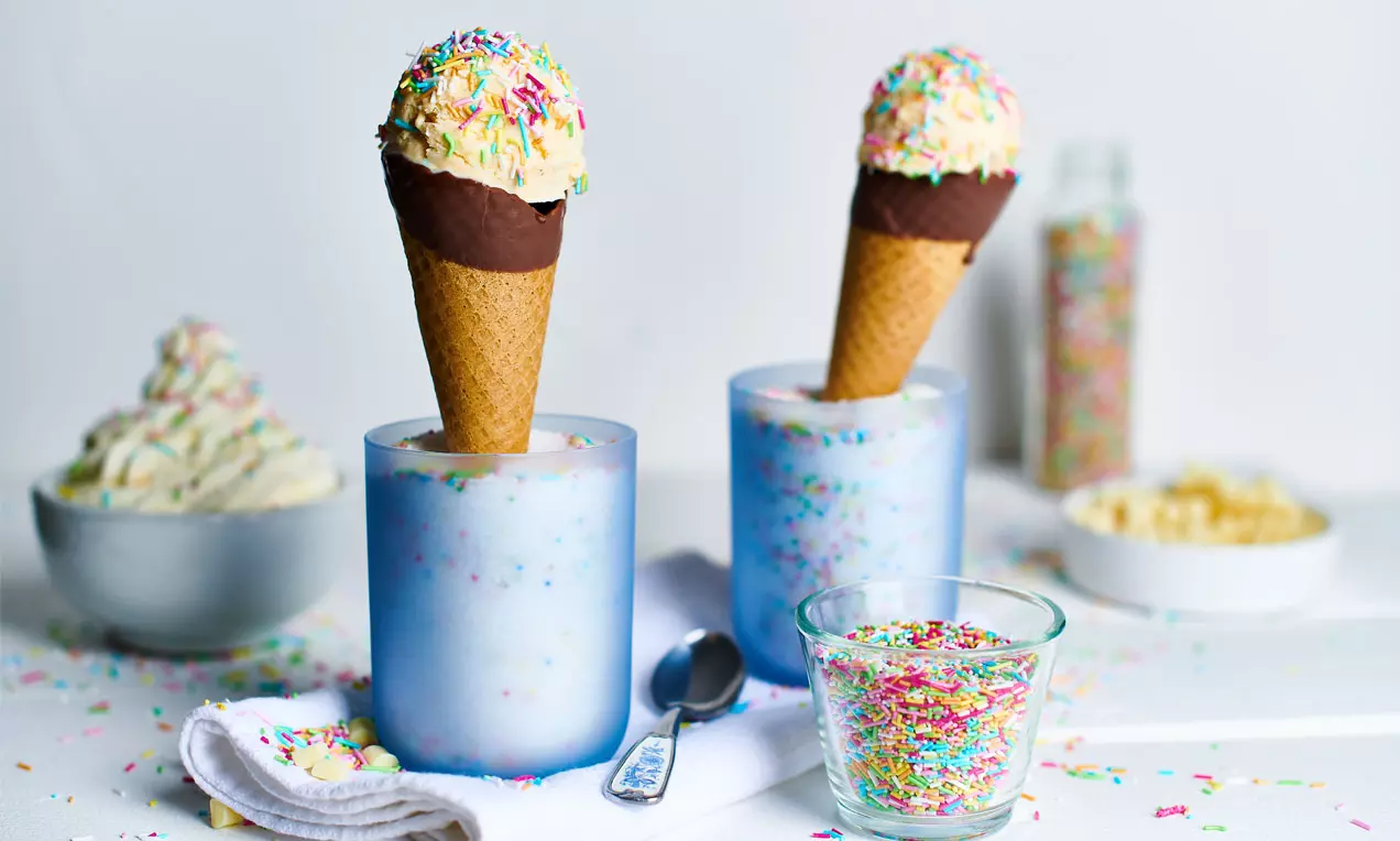 Vanilleeis mit bunten Zuckerstreuseln in einer mit Schokolade überzogenen Waffel, aufrecht in einem frostigen Glas arrangiert