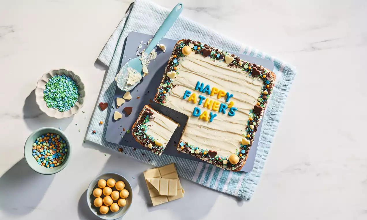 Oreo blondie with a pale cream topping, colourful sprinkles, chocolate edges, and letter decorations spelling "Happy Father's Day" on a baking tray