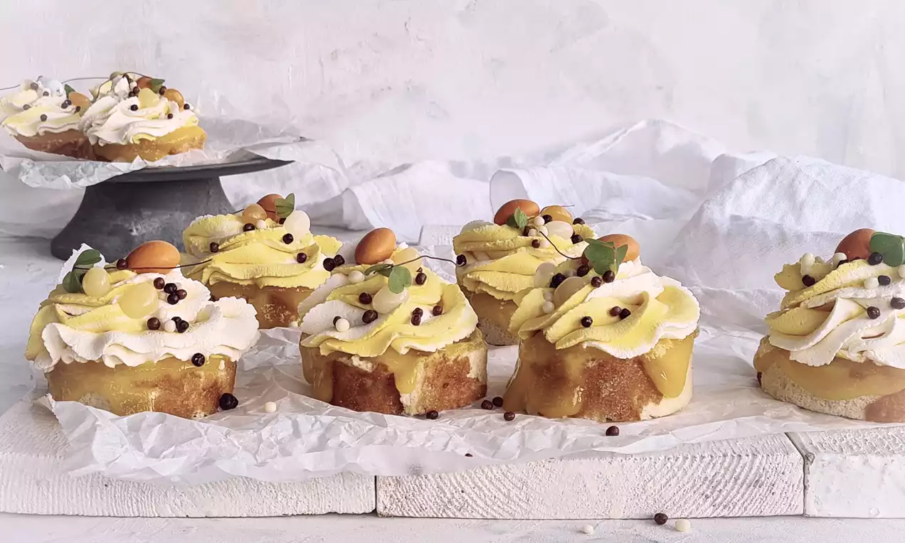 Kokosrullar med gyllene mangopuré toppade med krämig grädde, strössel och physalis på vitt bakplåtspapper på en ljus träyta