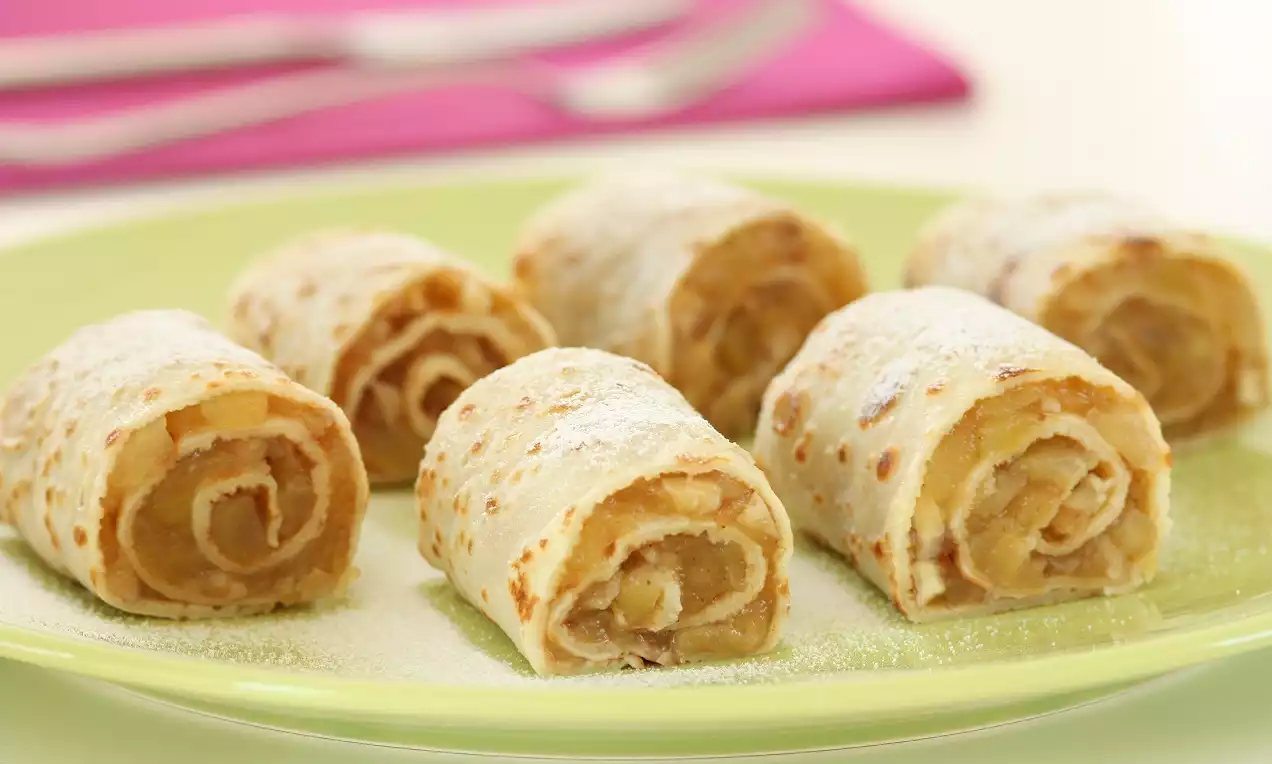 Altın rengi ince krep ruloları tarçın ve elma dolgulu, üzerine hafif pudra şekeri serpilmiş, parlak yeşil bir tabakta sunulmuş