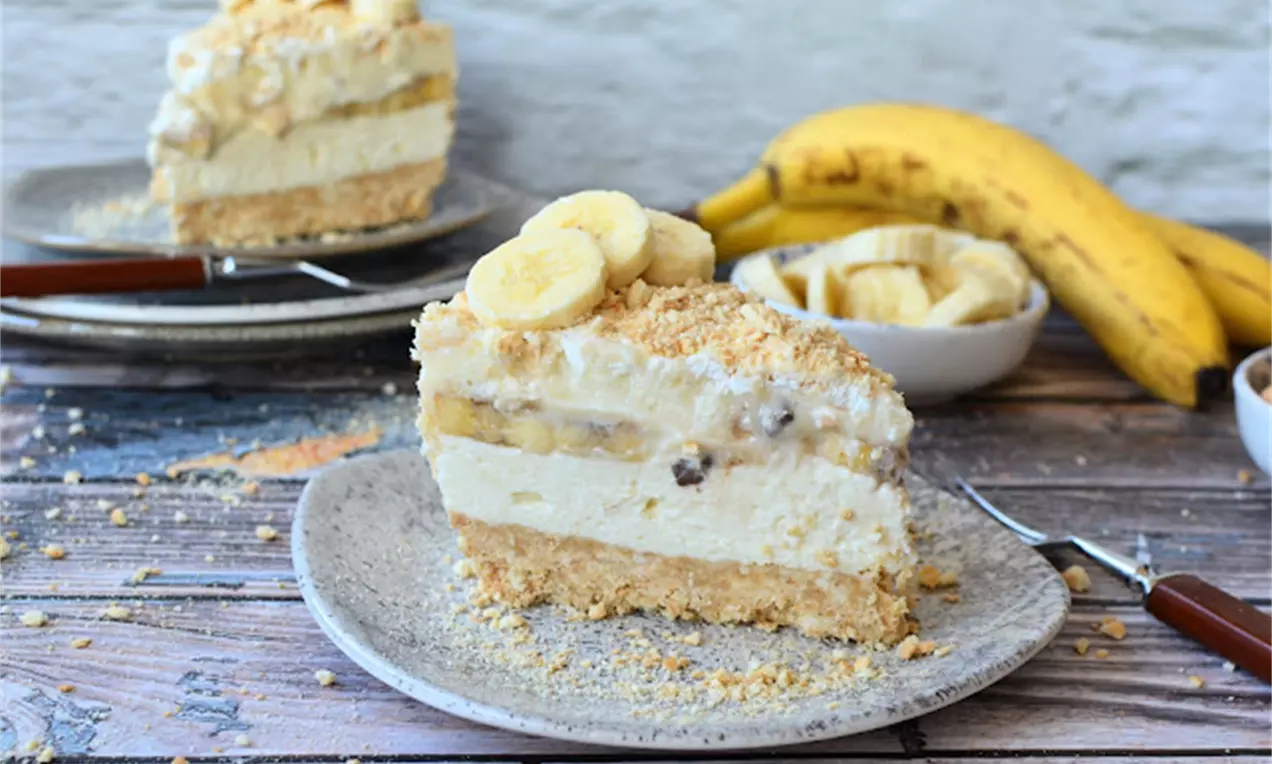 Парче бананова торта със слоеста текстура: бисквитен блат, кремообразна пълнеж с банани и поръски, гарнирано с парчета свеж банан