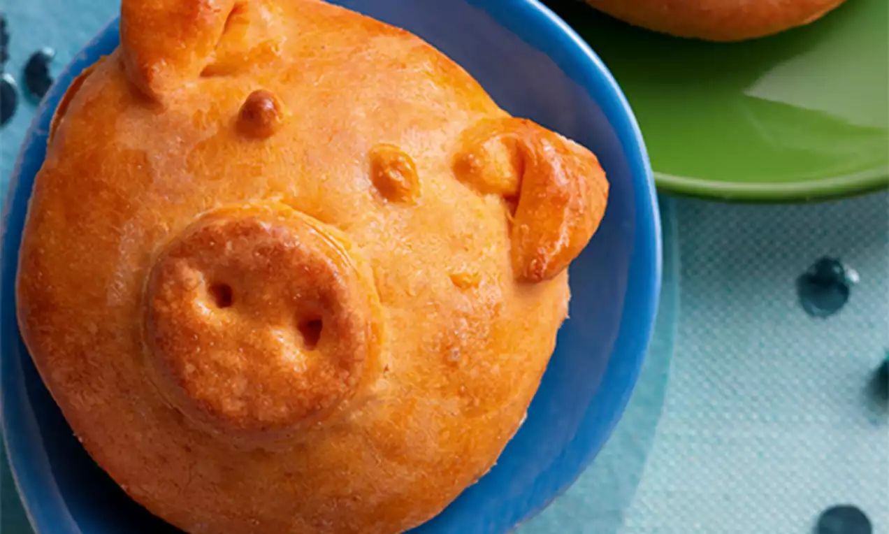 Petits pains dorés et brillants en forme de porcelets, disposés dans des assiettes colorées sur une nappe bleu clair ornée de perles décoratives