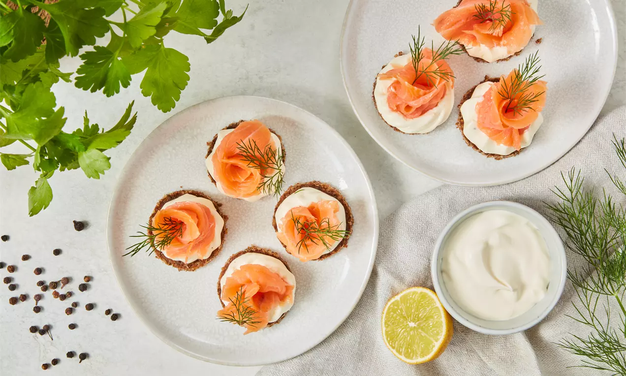 Canapés mit rosa Lachs auf heller Creme, garniert mit frischem Dill auf dünnen braunen Brot-Scheiben, dekoriert auf einem weißen Teller