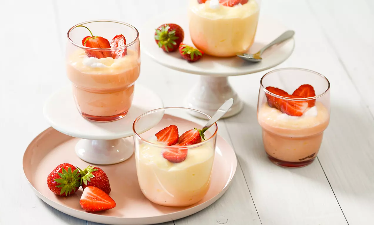 Pjenasti puding u čašama pastelnih tonova, ukrašen svježim polovinama jagoda, poslužen na bijelim i ružičastim tanjurima